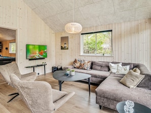 A modern living room with a pool table, comfortable seating, a flat-screen TV, and a large window with a view of greenery.