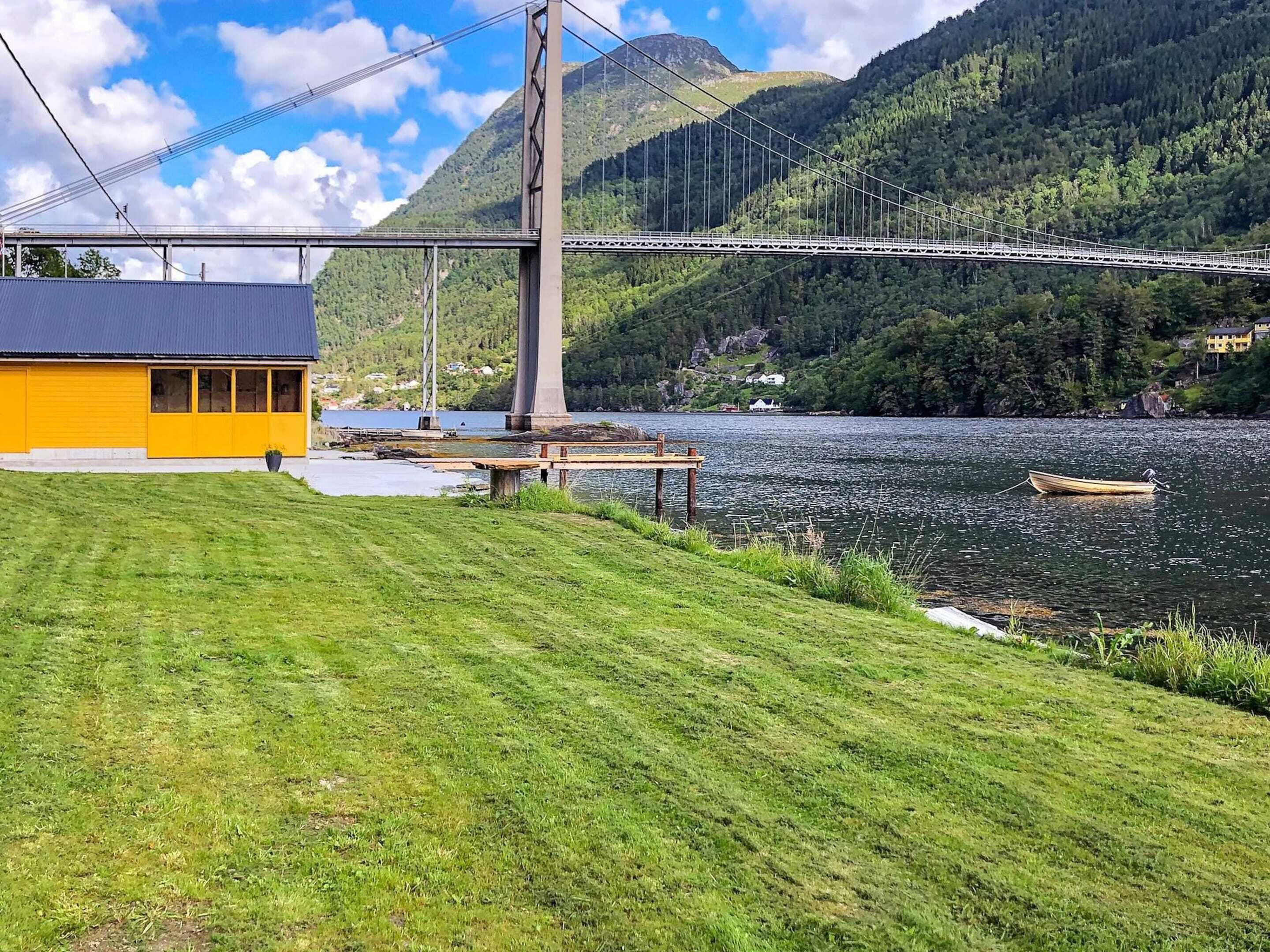 A suspension bridge over a river, a grassy area, and a yellow building.