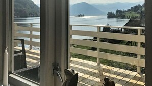 Ein Balkon mit kariertem Boden, weißer Brüstung und Blick auf einen See mit Bergen im Hintergrund.