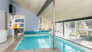 Una piscina interior con paredes de vidrio transparente, un banco azul y un poste metálico.