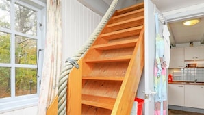 Una escalera de madera con barandilla de cuerda que lleva a una zona de cocina con armarios y un fregadero.