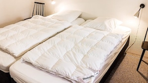 Una cama doble con ropa de cama blanca y etiqueta de colchón DUNLOO. Hay dos lámparas de pared a cada lado de la cama.