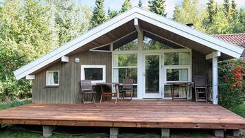A wooden cabin with a deck, large windows, and a covered patio area.