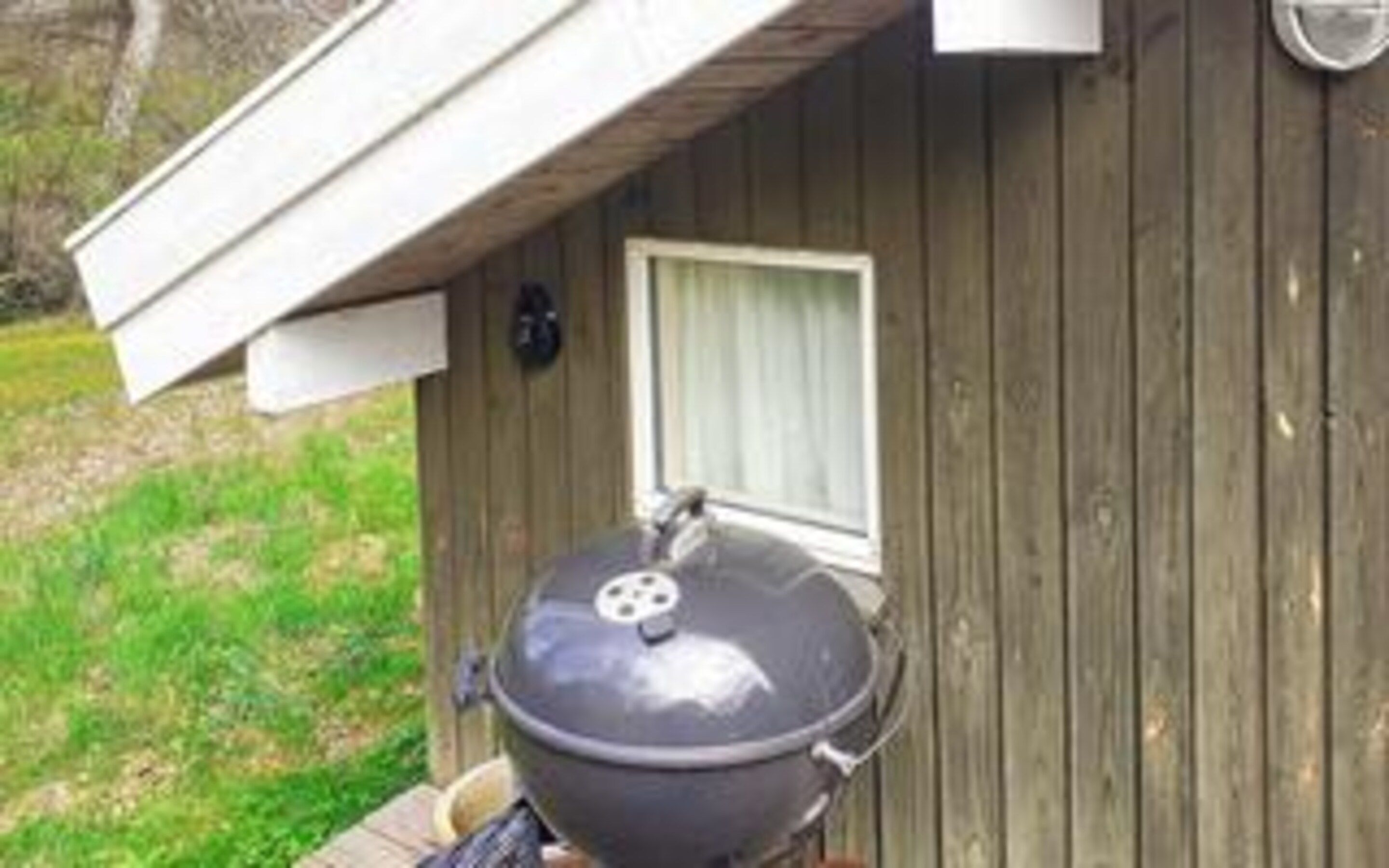 A barbecue grill outside a wooden building with a window and a door.