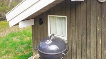 A barbecue grill outside a wooden building with a window and a door.
