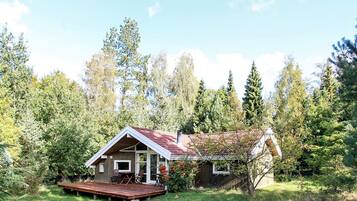 A wooden cabin with a deck, surrounded by trees and a clear sky.