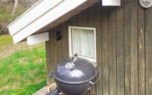 En grill tilgængelig udenfor en træbygning med et vindue og en dør.