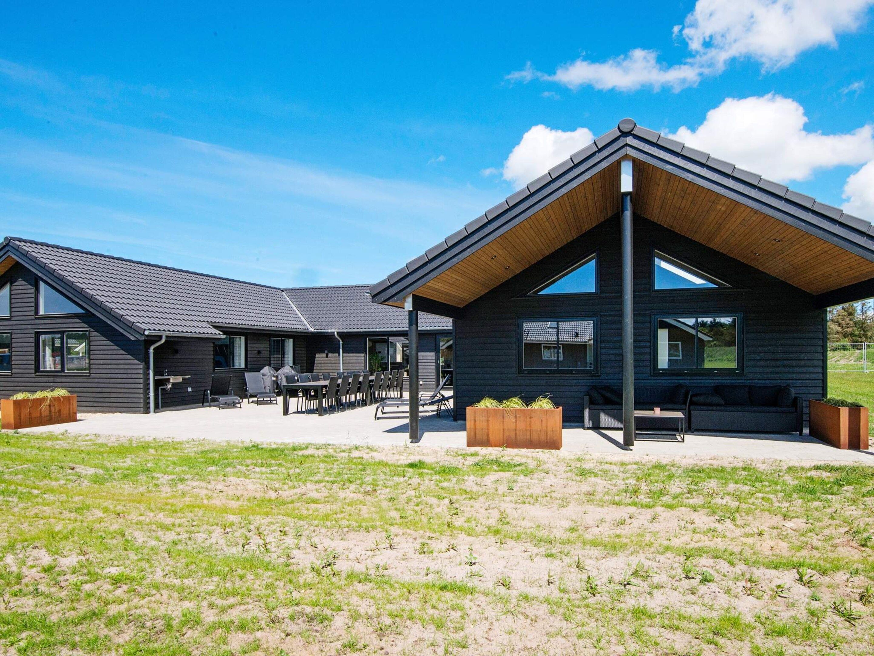 A modern building with a covered patio area, outdoor seating, and a grassy field in the foreground.
