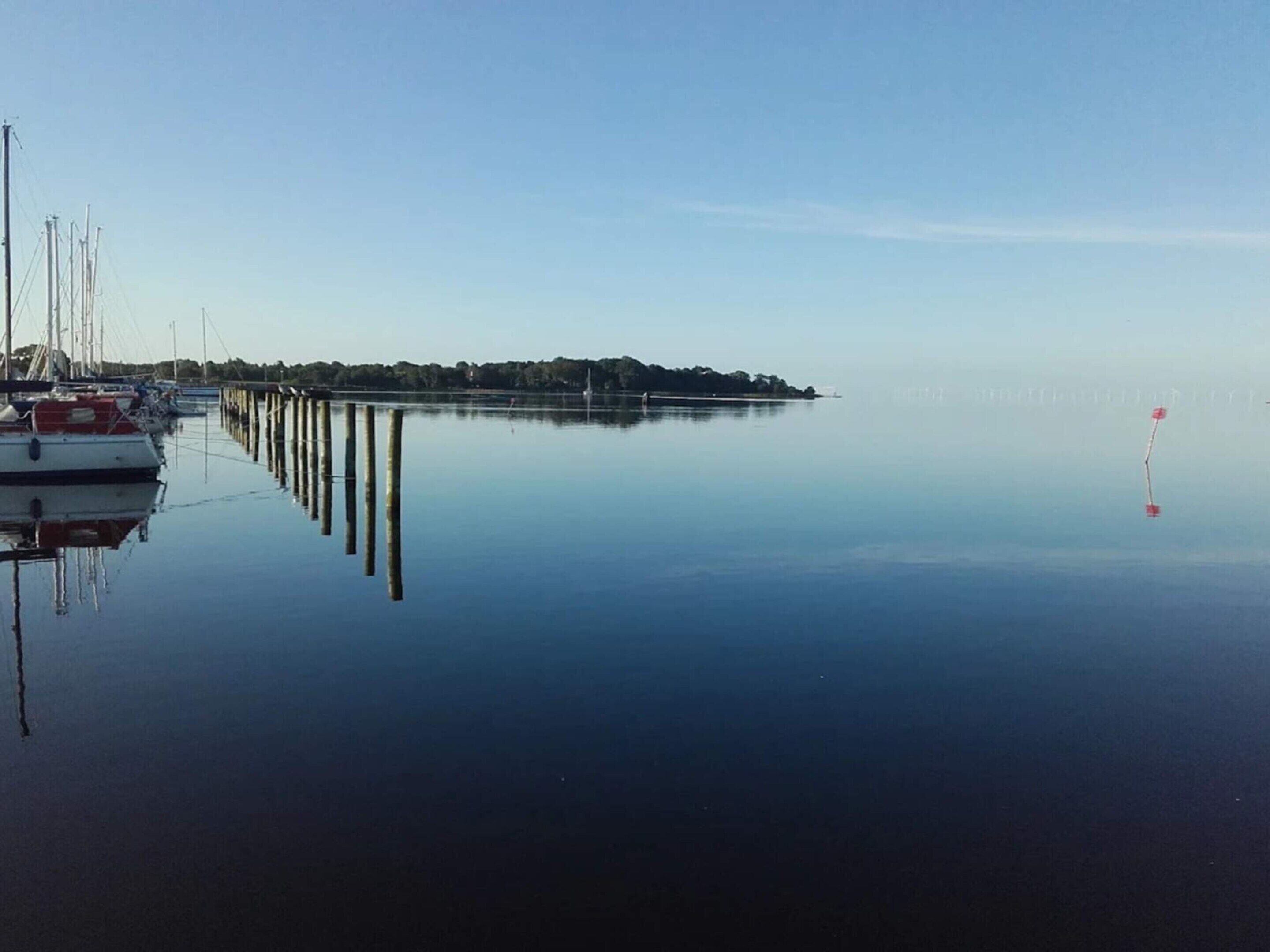 A calm marina with boats docked, a pier extending into the water, and a distant shoreline.