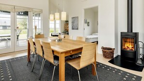 A modern dining area with a wooden table and chairs, a fireplace, and a view through large windows. - 4 Star Holiday Home in Nysted (Nysted)