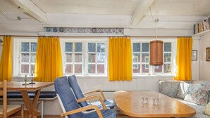 A room with a wooden dining table, a blue chair, a sofa, and yellow curtains. - Traditional Holiday Home in Jutland near Sea (Fano)