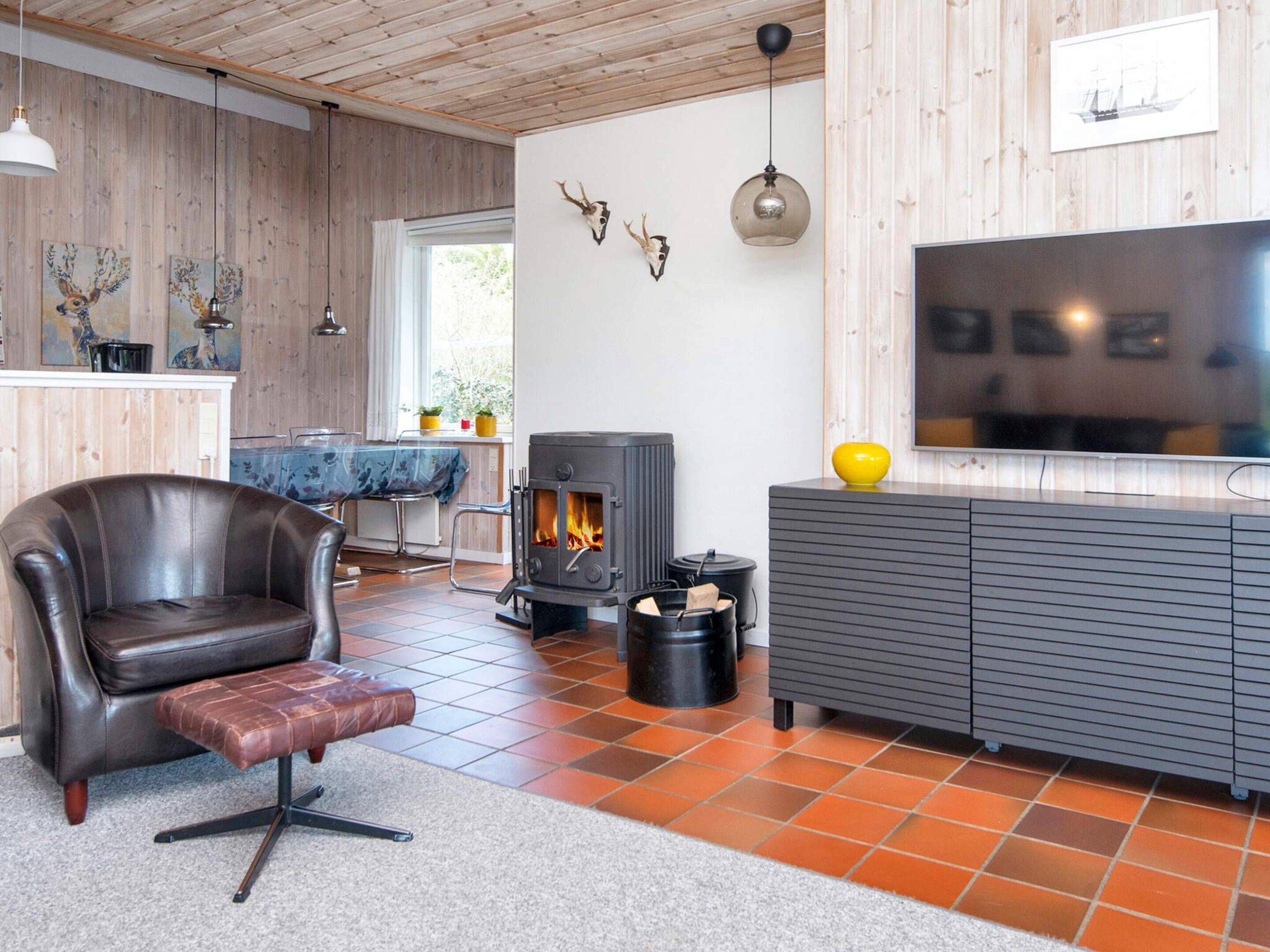 A modern living room with a leather armchair, a fireplace, a television, and wooden walls.
