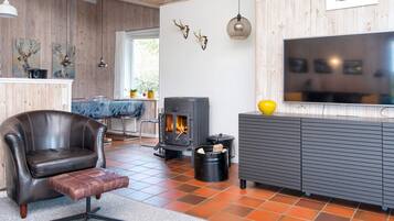 A modern living room with a leather armchair, a fireplace, a television, and wooden walls.