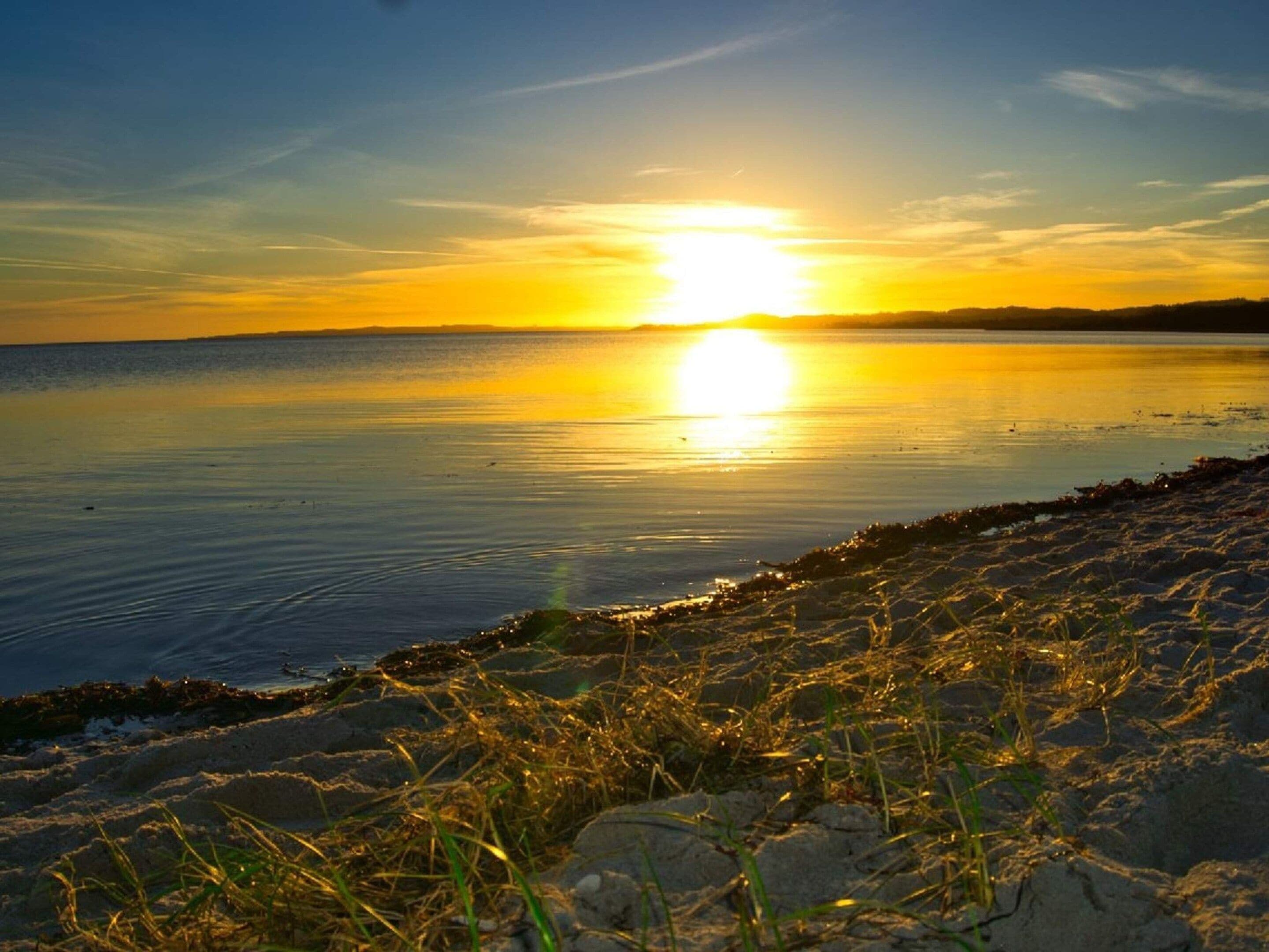 A sunset over a calm body of water with a rocky shoreline in the foreground.