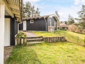 A black wooden house with a white door, a satellite dish, and a small garden with steps leading to the entrance. - 8 Person Holiday Home in Ebeltoft (Ebeltoft)
