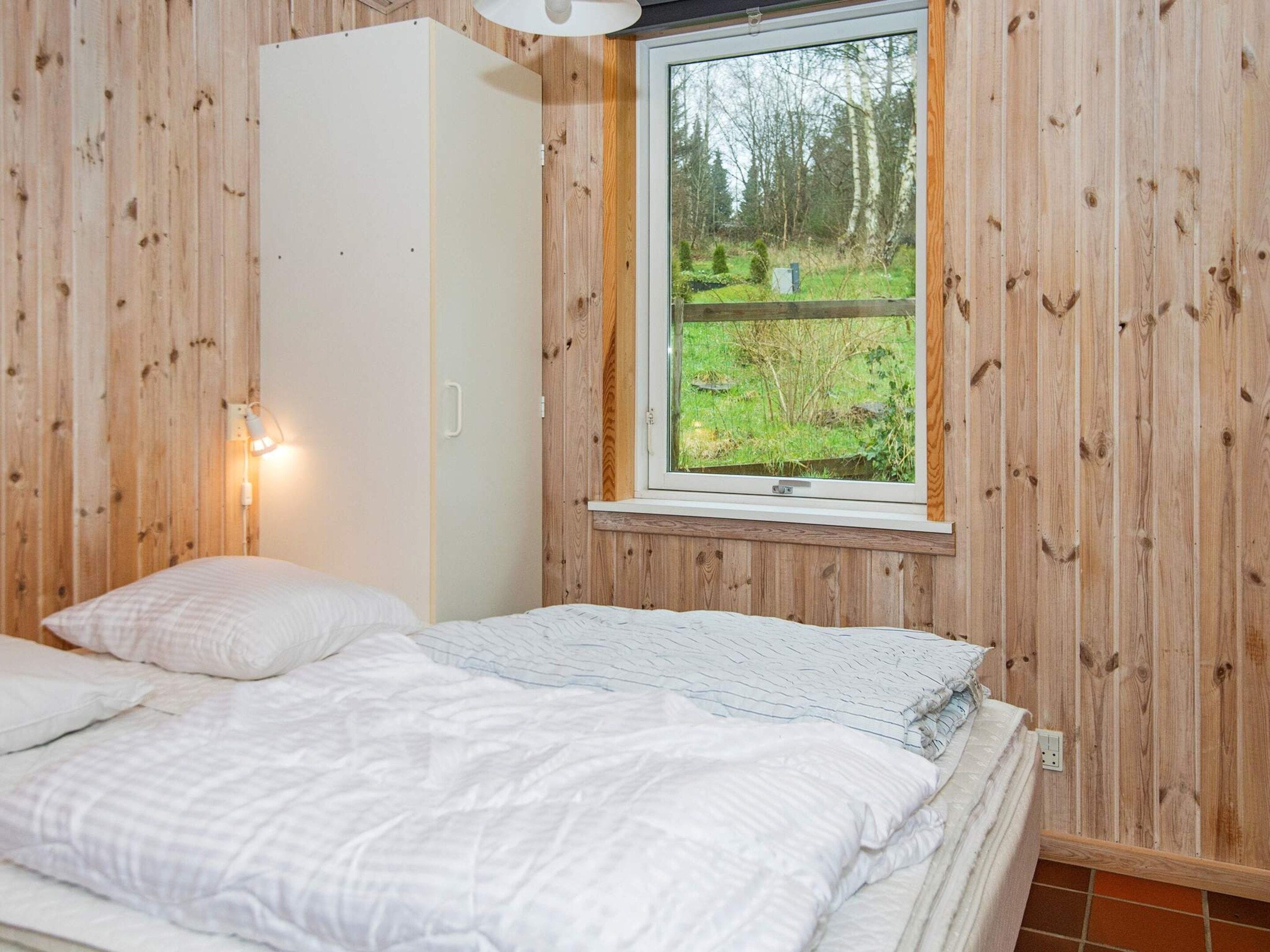 Quarto com cama, guarda-roupa e janela com vista para uma floresta.