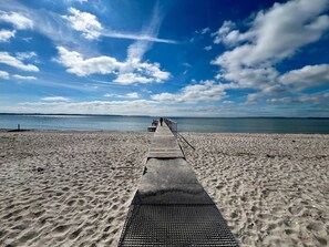 Pasarela de madera que conduce a una playa con cielo despejado y mar tranquilo.