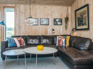 A room with a brown leather sofa, a round white coffee table, and a hanging plant.