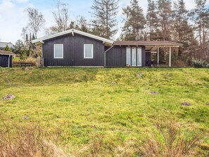 A dark wooden house with two windows and a covered porch. - 8 Person Holiday Home in Ebeltoft (Ebeltoft)