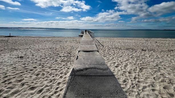 Pasarela de madera que conduce a una playa con cielo despejado y mar tranquilo.
