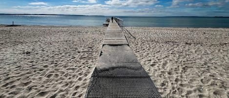 A beach with a wooden walkway leading to the water, a metal railing, and a clear sky.