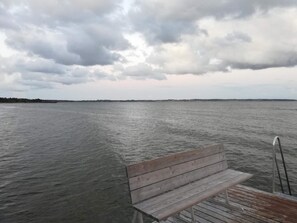 A wooden bench on a pier with a view of a calm body of water and a distant shoreline. - 8 Person Holiday Home in Ebeltoft (Ebeltoft)