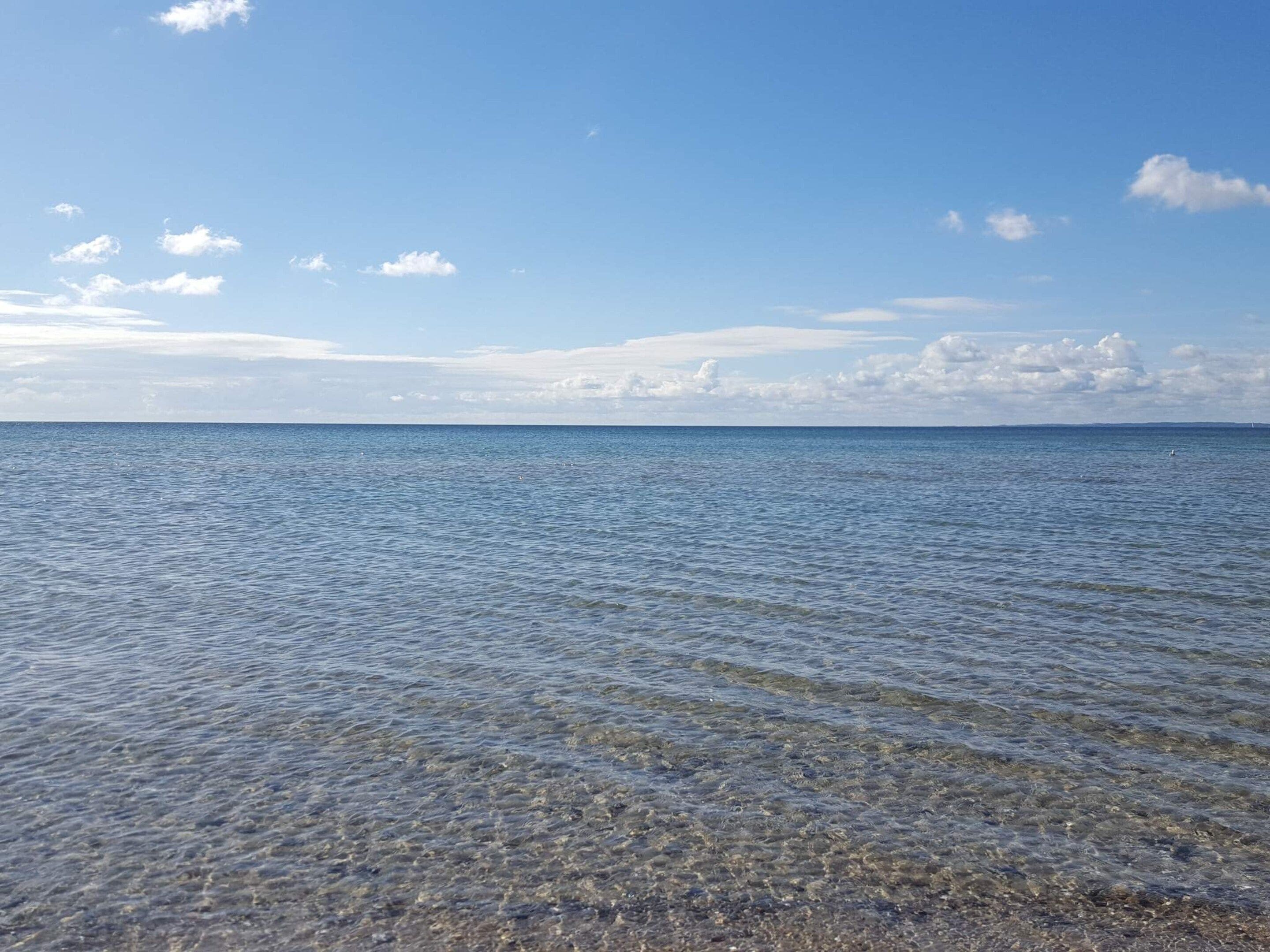 Une vue dégagée sur une mer calme aux vagues douces, un ciel clair et un horizon lointain.