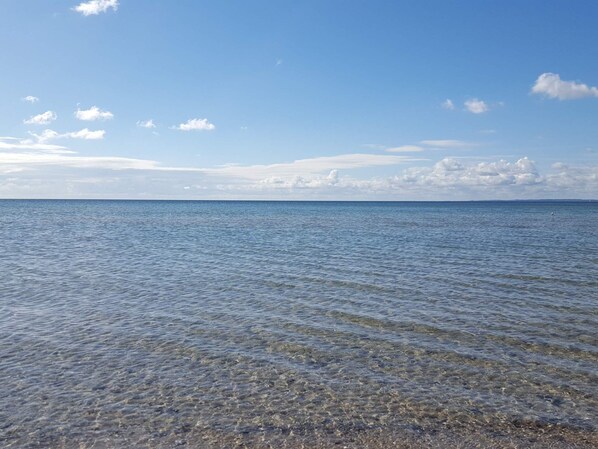 A clear view of a calm sea with gentle waves, a clear sky, and a distant horizon.
