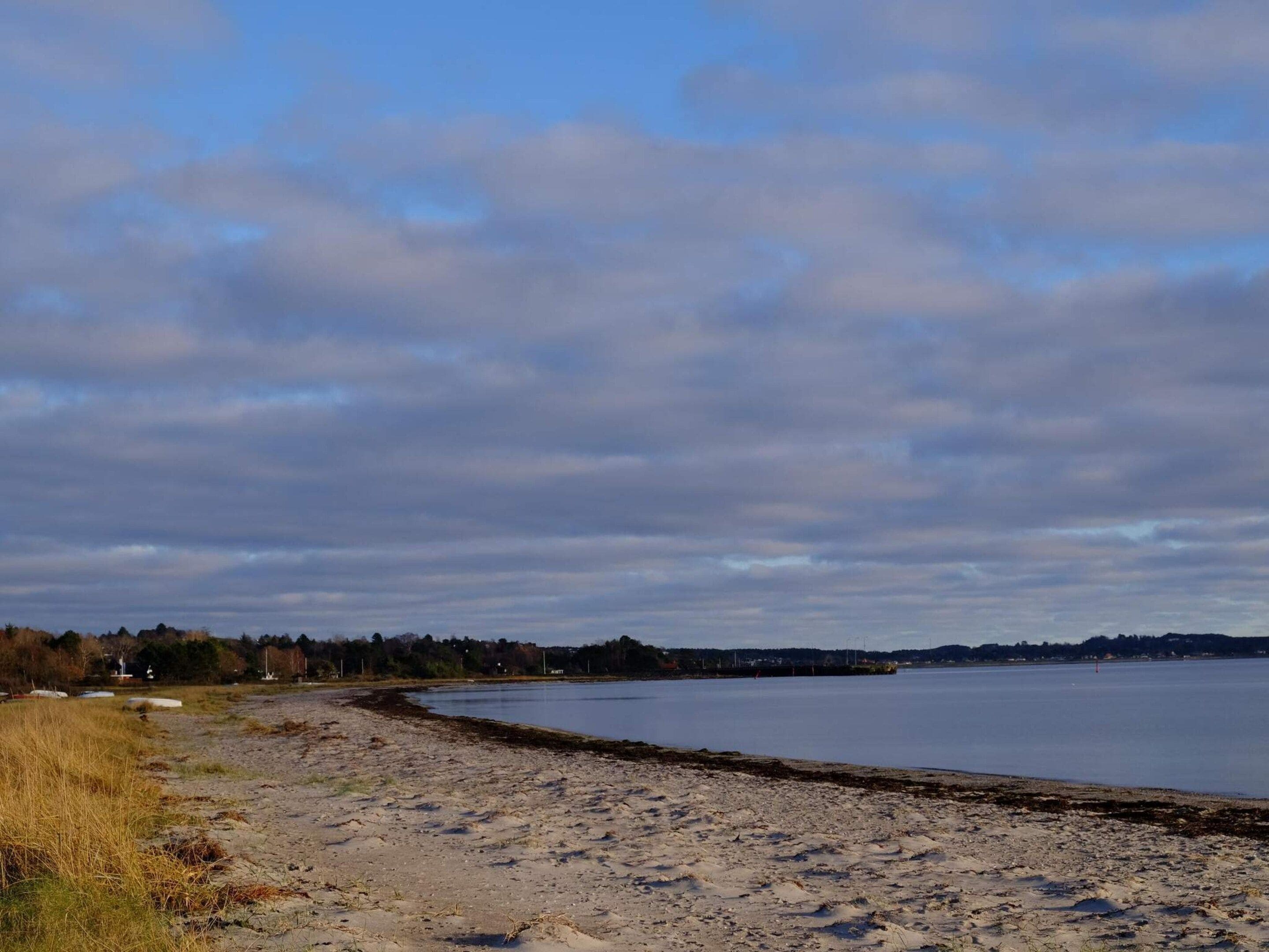 A beach with a sandy shore, a calm body of water, and a cloudy sky.