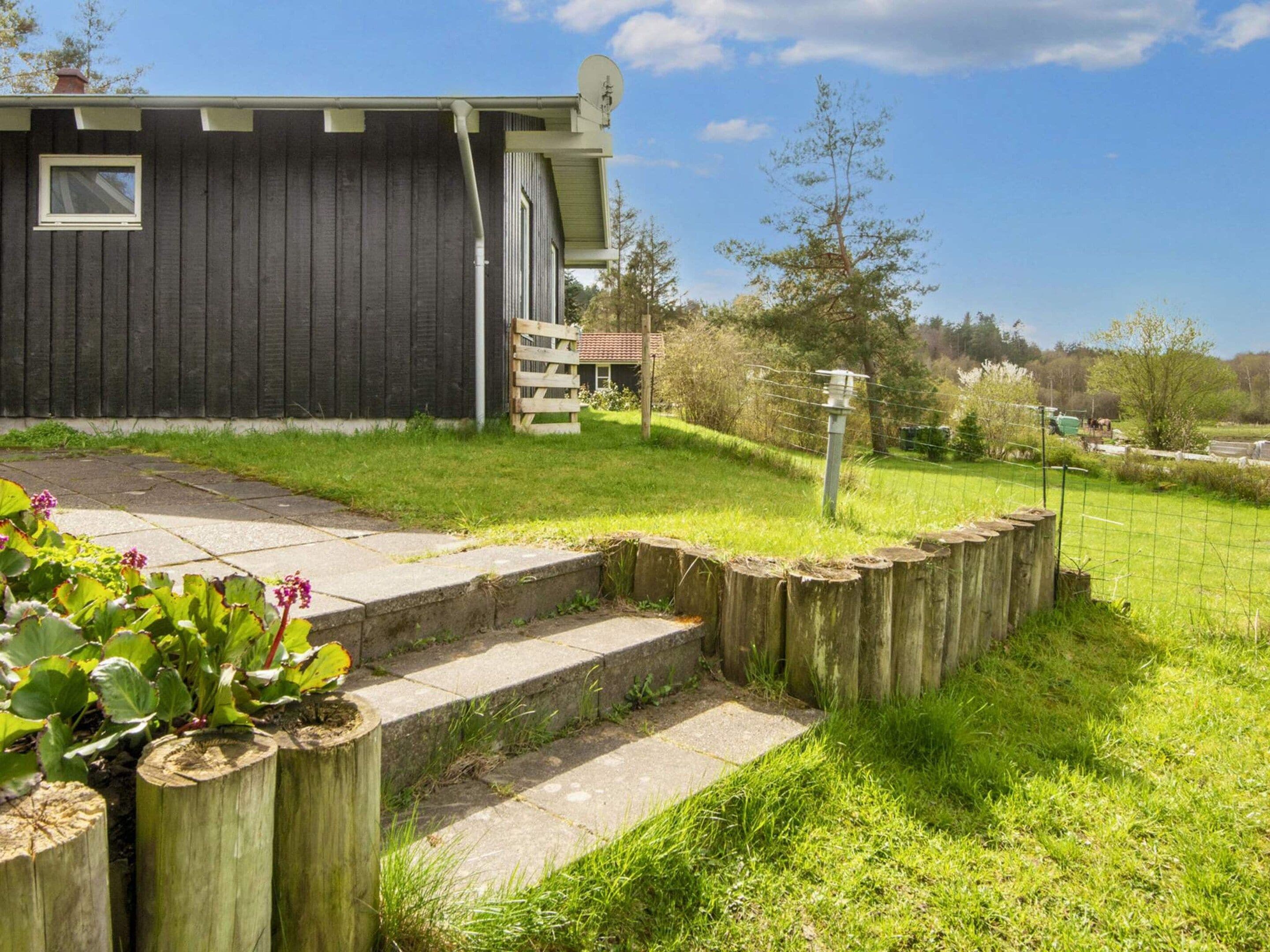 A house with a dark exterior, a satellite dish, a wooden fence, and a grassy yard.