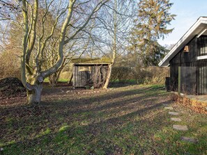 A rustic wooden structure with a tiled roof, surrounded by a natural landscape with trees and a stone pathway. - 4 Person Holiday Home in Praesto (Praesto)