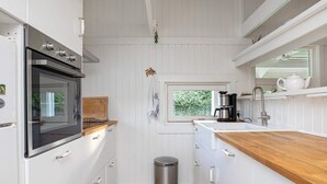 A modern kitchen with white cabinetry, a wooden countertop, a stainless steel oven, a coffee maker, and a window with a view of greenery. - 4 Person Holiday Home in Praesto (Praesto)