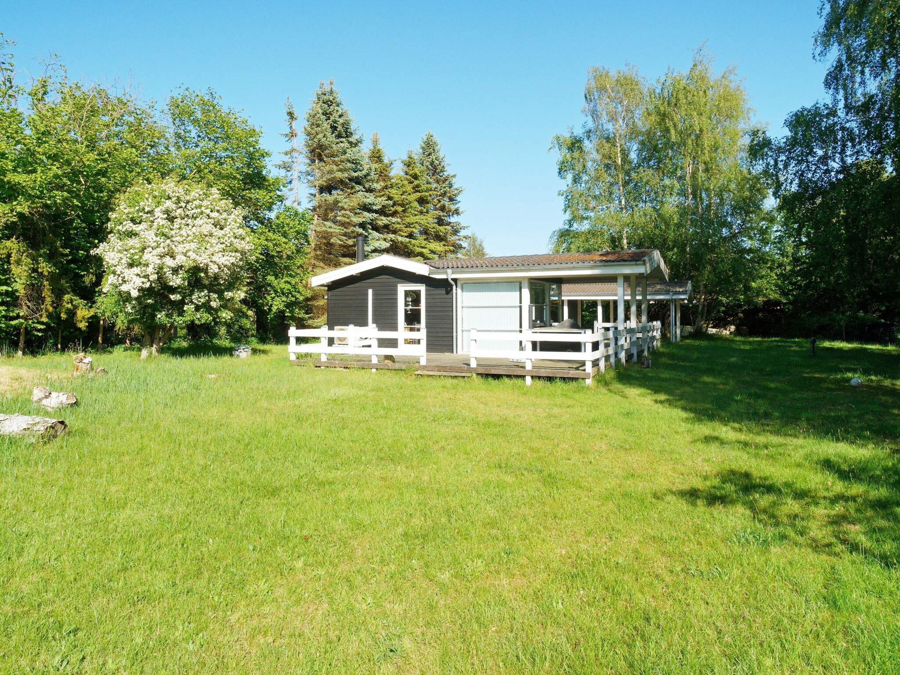 Une maison de plain-pied avec un porche, entourée d’une cour verdoyante et d’arbres.