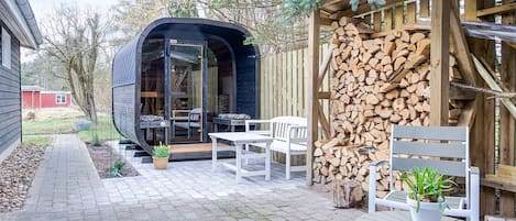 A modern outdoor seating area with a curved structure, a stack of firewood, and a potted plant.