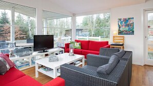 A modern living room with a red sofa, grey wicker sofa, and a white coffee table. There is a TV on a white stand, and a painting on the wall. - Simplistic Holiday Home in GÃ¸rlev near Sea (Gørlev)