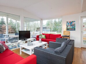 A modern living room with a television, red and grey furniture, a white coffee table, and large windows offering a view of the outdoors. - Simplistic Holiday Home in GÃ¸rlev near Sea (Gørlev)