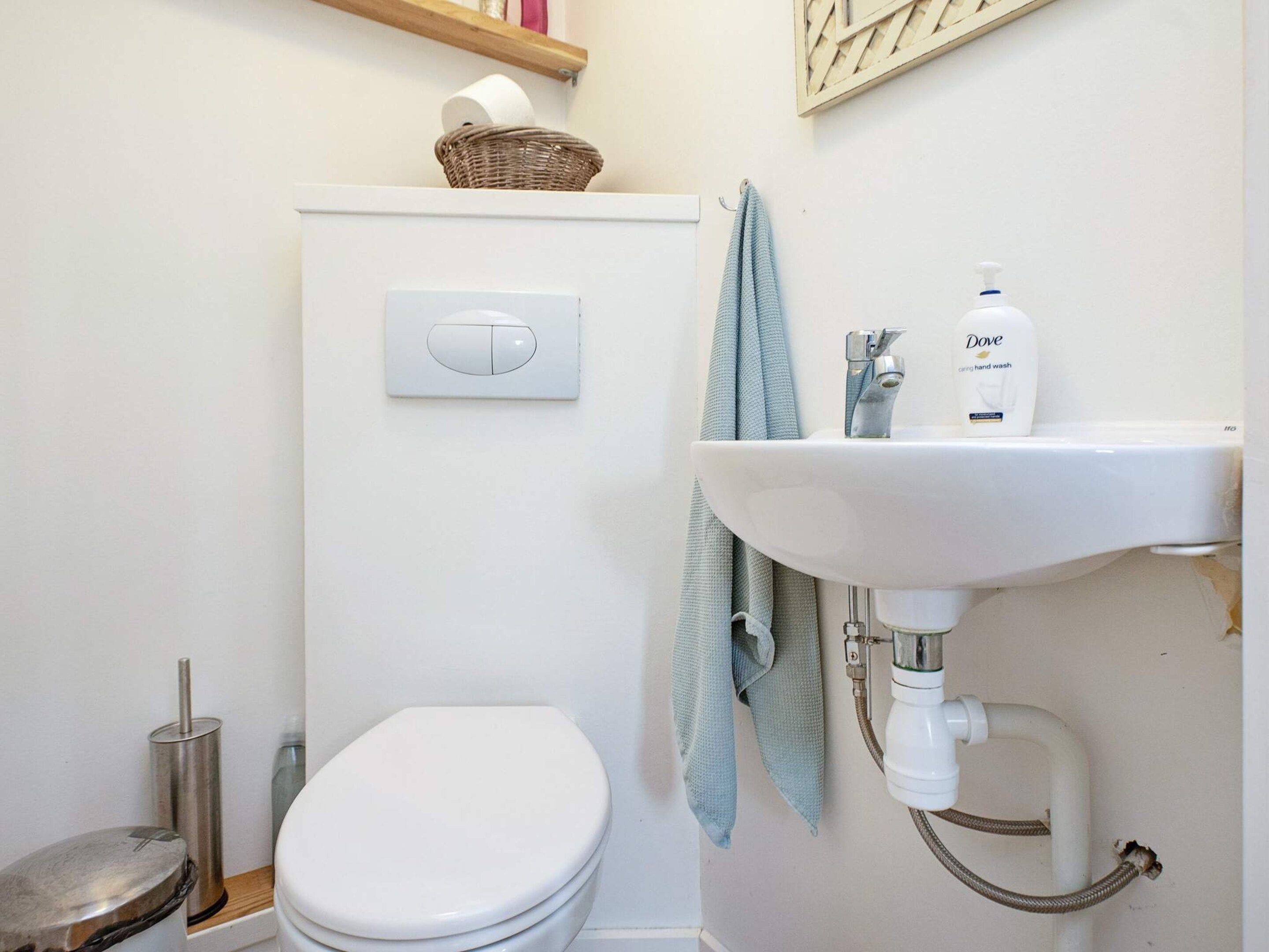 A bathroom with a toilet, a sink, a hand soap dispenser, and a towel hanging on the wall.
