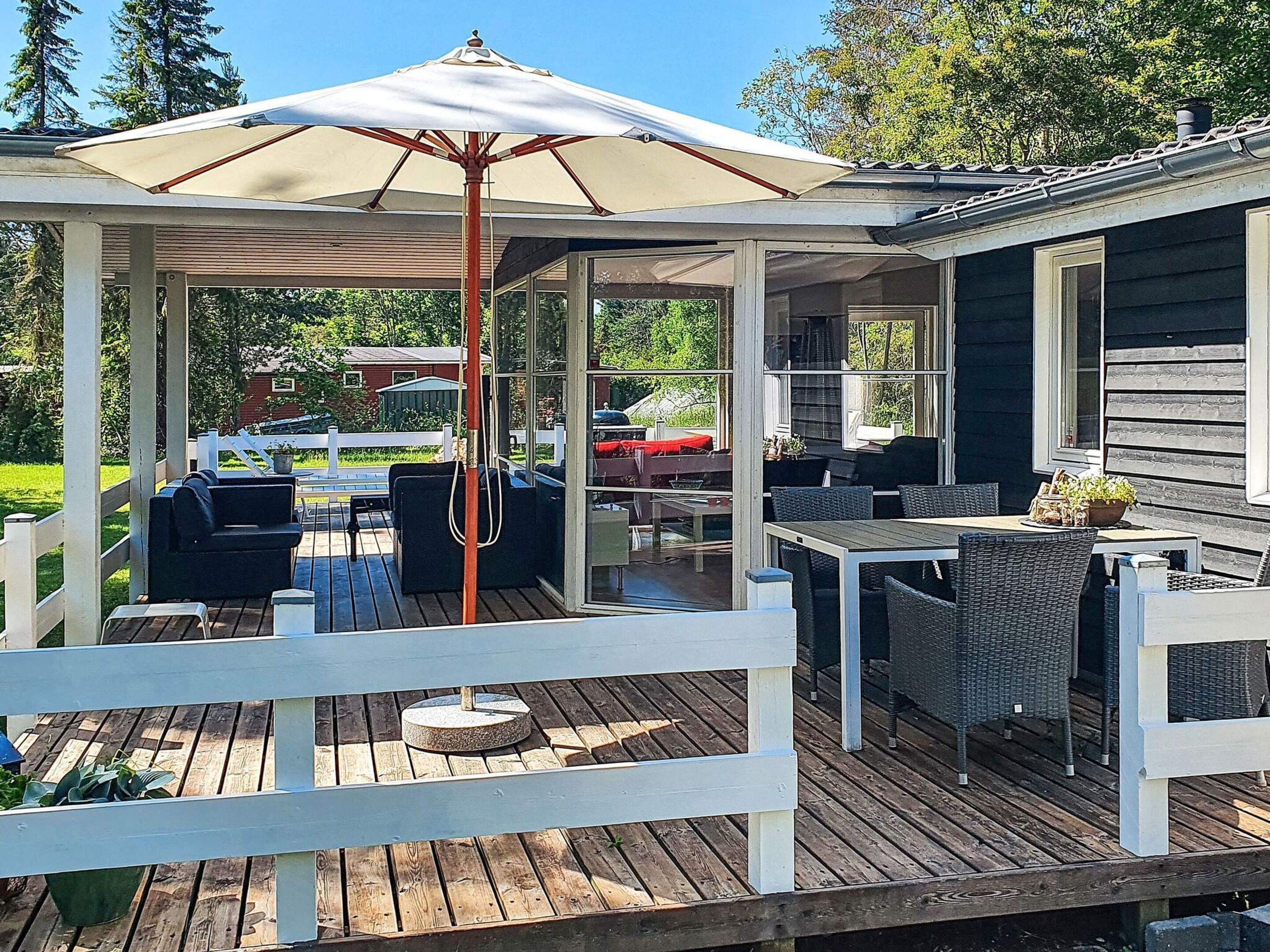 Un patio techado al aire libre con una mesa y sillas, cerca blanca y vista al jardín trasero.