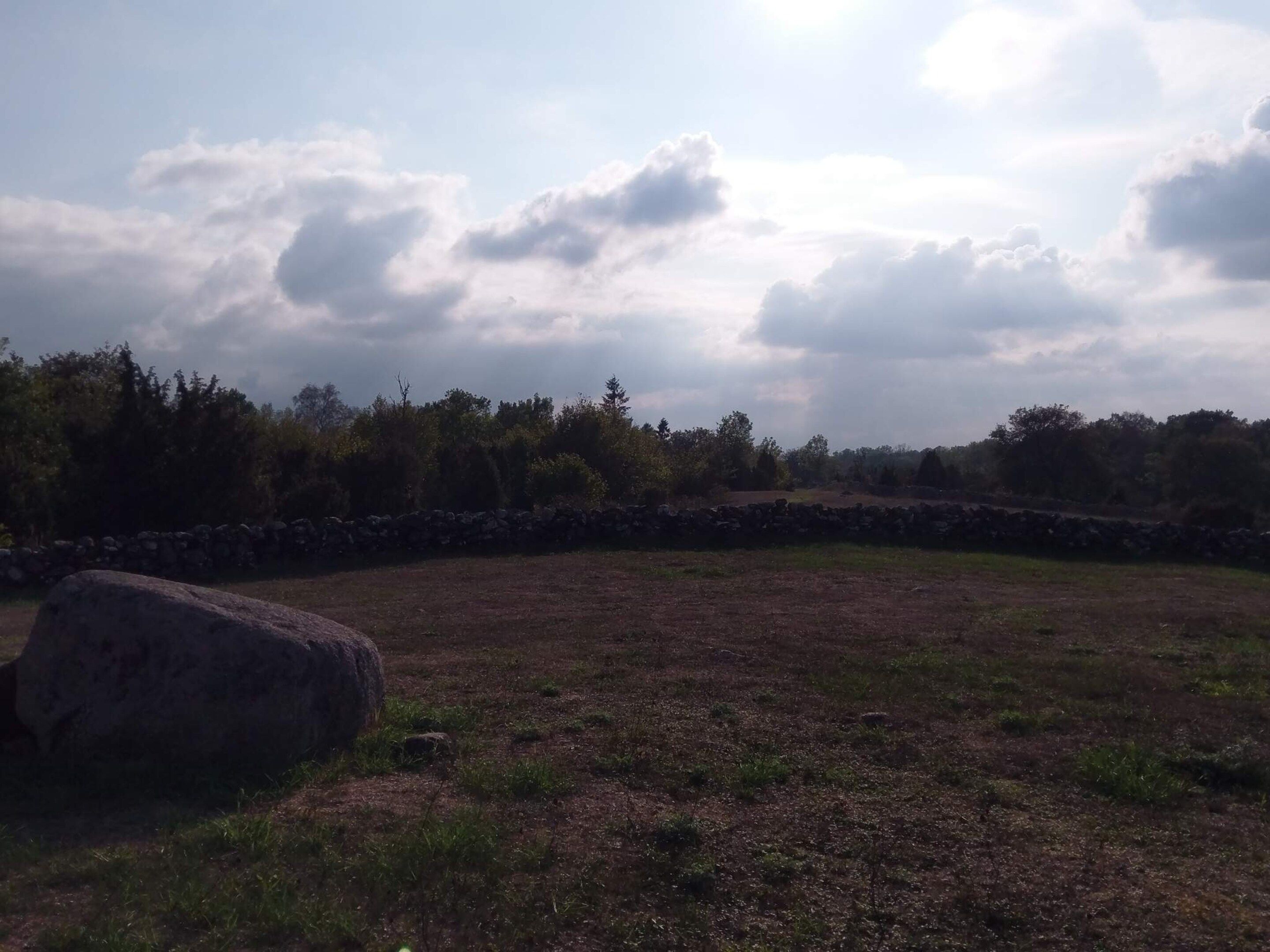 An open field with a stone wall and a large rock.