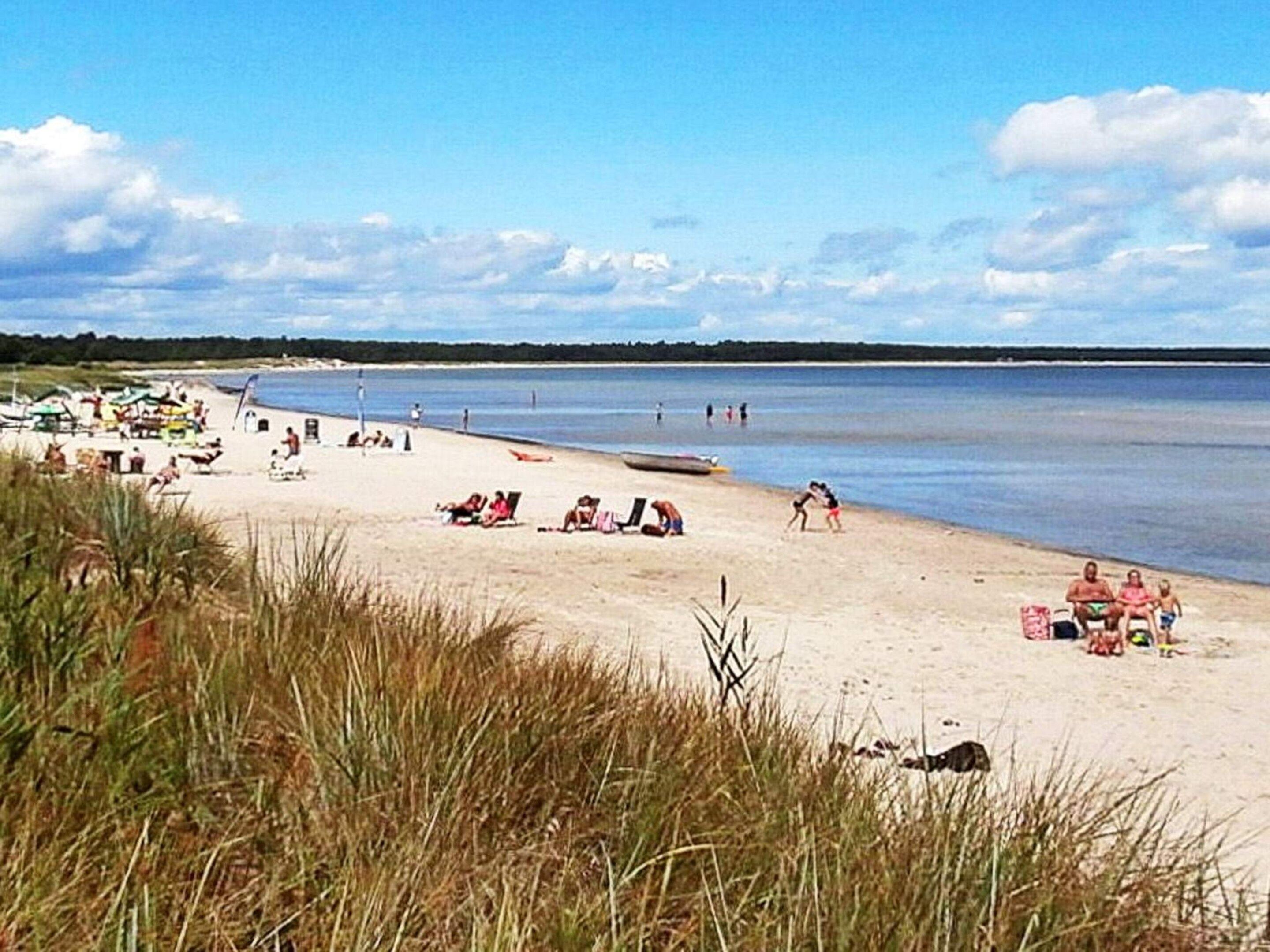 A beach with people sunbathing and swimming, a boat on the water, and a clear sky.