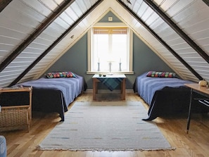 A small attic bedroom with two beds, a table, and a window.