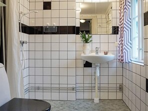 Features a pedestal sink, shower with glass door, and a window with a patterned curtain.