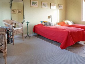 Una habitación con dos camas, una silla de mimbre, una lámpara de pie y una obra de arte en la pared.