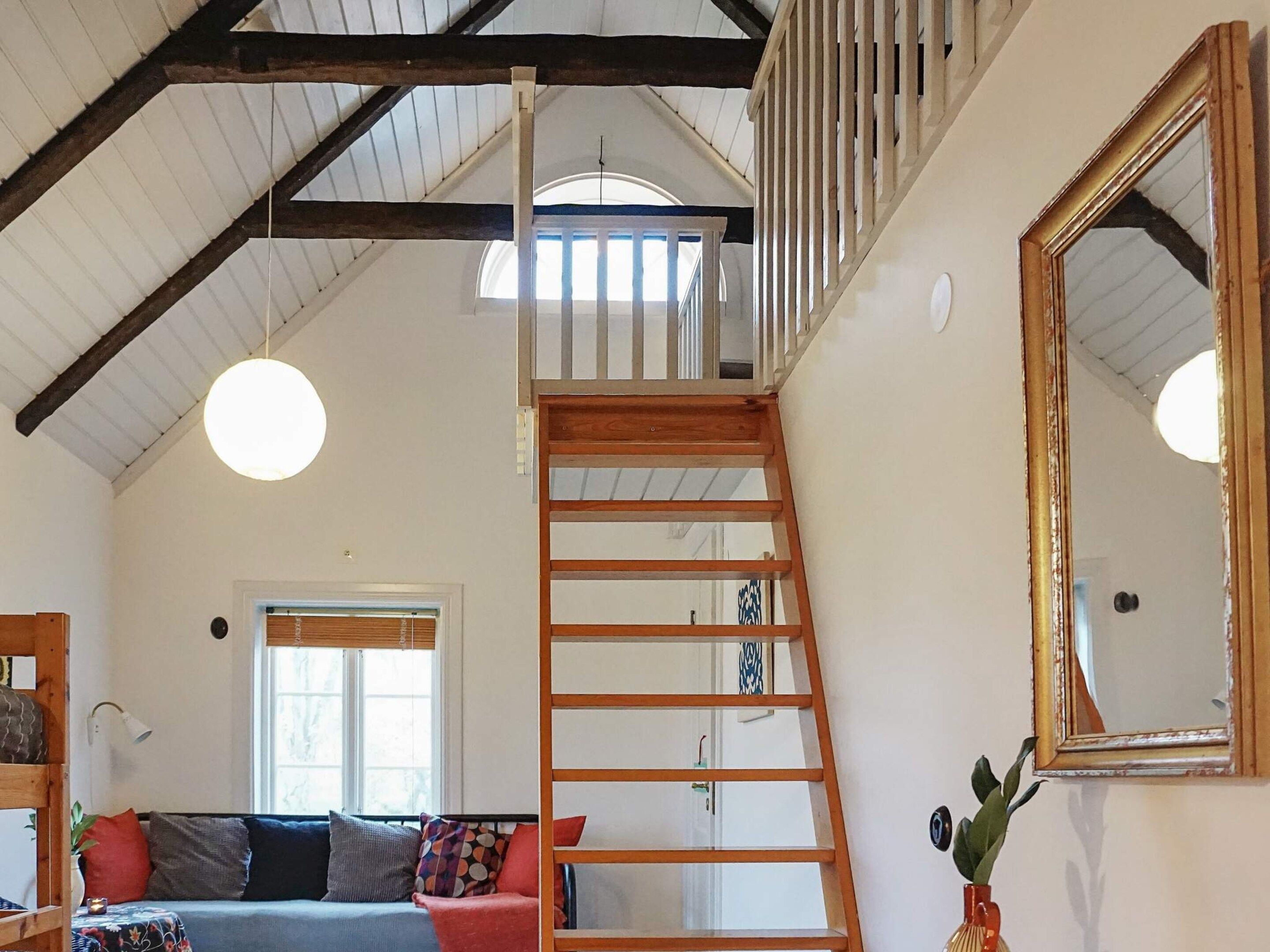 A loft-style room with a wooden staircase, a large mirror, and a sofa with cushions.