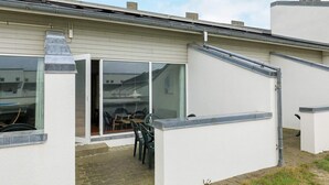 A modern house with a covered patio, a sliding glass door, and a small outdoor seating area. - 6 Person Holiday Home in Brovst (Brovst)