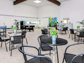 Un espacio interior amplio con varias mesas y sillas, una mesa de billar y plantas en macetas.