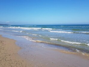 A beach with waves, a clear sky, and distant land. - 6 Person Holiday Home in Brovst (Brovst)