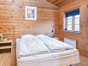 A wooden cabin room with a bed, a nightstand, a lamp, a window, and a framed picture on the wall. - Captivating Holiday Home in RingkÃ¸bing near Sea (Ringkobing)