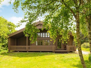 A wooden cabin with a porch, surrounded by trees and grass. - Captivating Holiday Home in RingkÃ¸bing near Sea (Ringkobing)