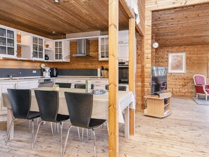 A modern kitchen with white cabinetry, a dining table with four chairs, and a television on a wooden stand. - Captivating Holiday Home in RingkÃ¸bing near Sea (Ringkobing)